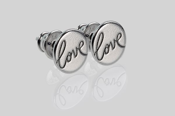 Makro Produktaufnahme von zwei Silber Ohrsteckern mit dem Prägung LOVE auf spiegelndem Untergrund