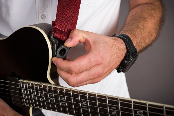 Fotostudio Wertbeaufnahme von einer schwarzen E-Gitarre mit rotem Gitarrengurt in der hand eines Gitarristen